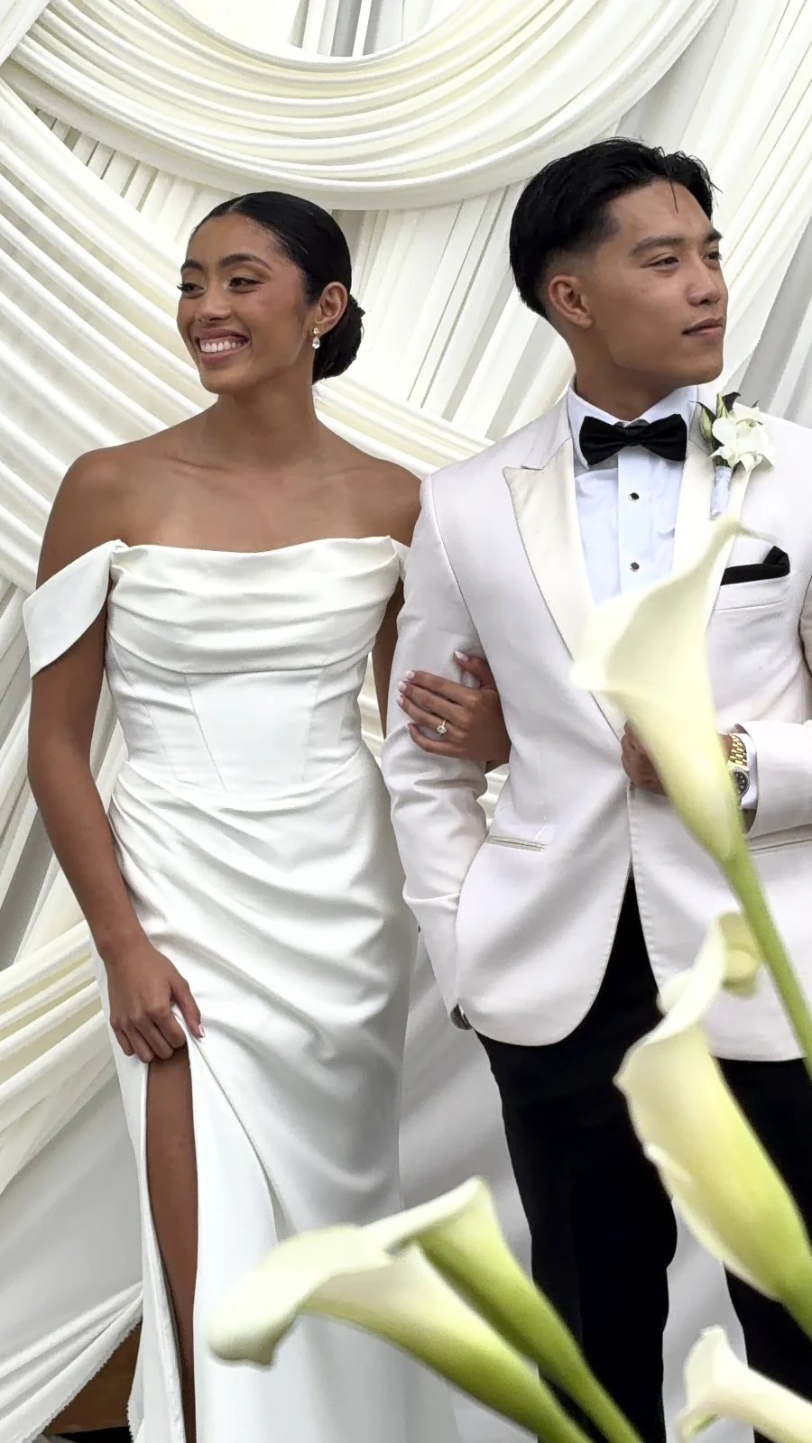 Newlyweds smiling together in front of white drapery